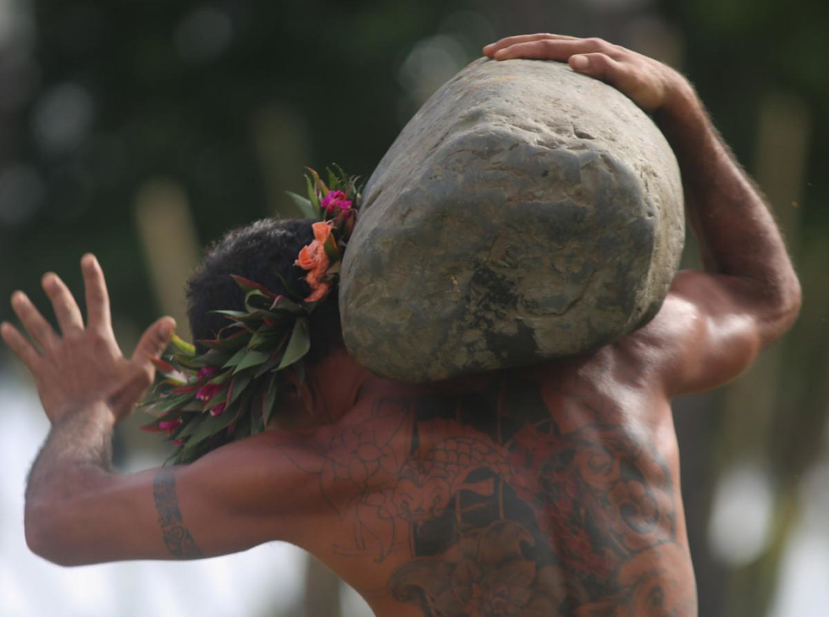 A man balances a large stone on his shoulder