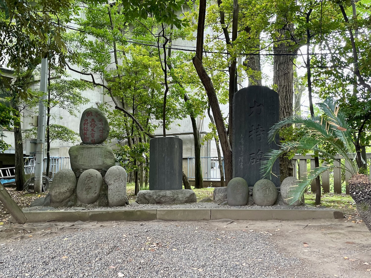 A photo of the chikaramochi monument. two sets of three lifting stones are mounted facing towards the viewer. A final seventh stone is mounted on a plinth above the first set of three on the left hand side.