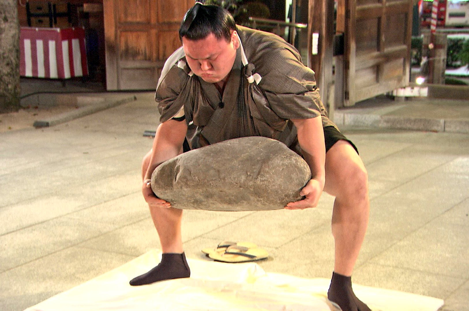 A sumo wrestler is lifting a stone.