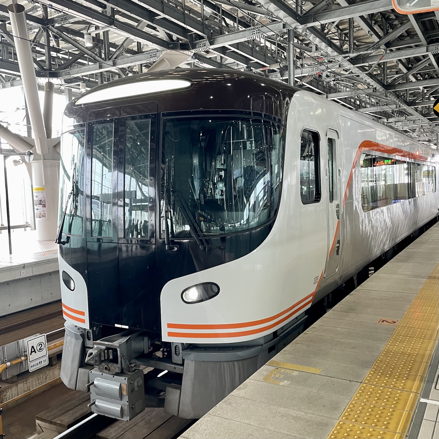 A white train with large windows waits at its platform.