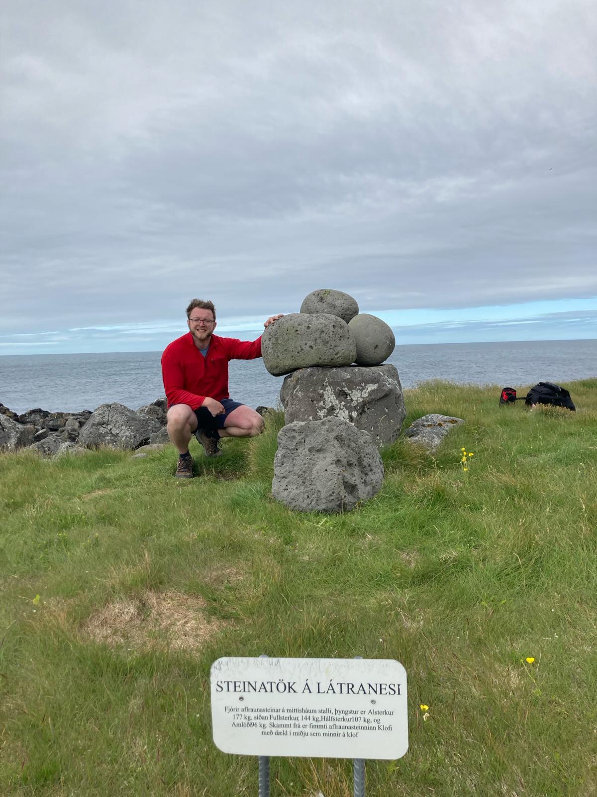 Jacob squats down next to a group of stones sat on a plinth at Latra in Iceland
