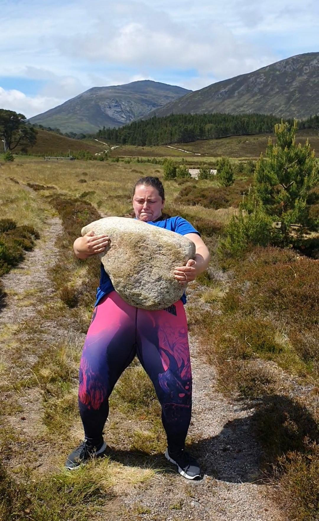 A woman standing up and leaning back while gripping a heavy stone.
