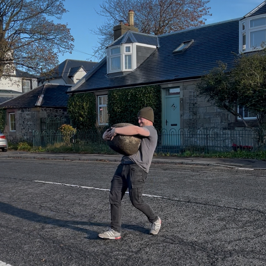 David Brodlie carries the Loans Stone across the main road with the stone tightly pulled into his chest.