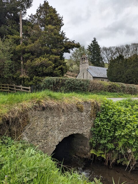 A stone road bridge crosses over a narrow stream, the church is visible in the background.
