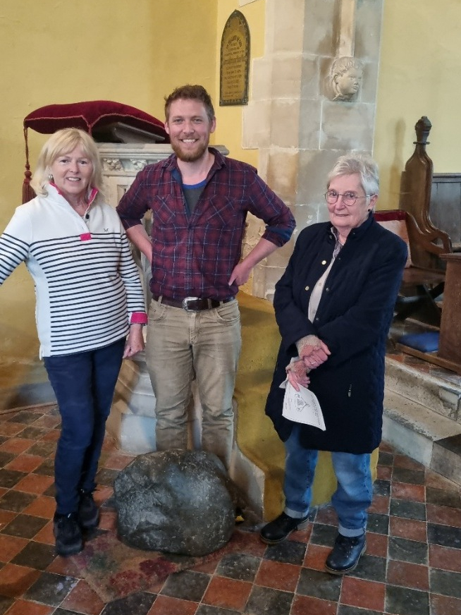 Three people stand next to the stone at the pulpit. The stone is sat on a small piece of carpet or a door mat to protect the tiled floor.