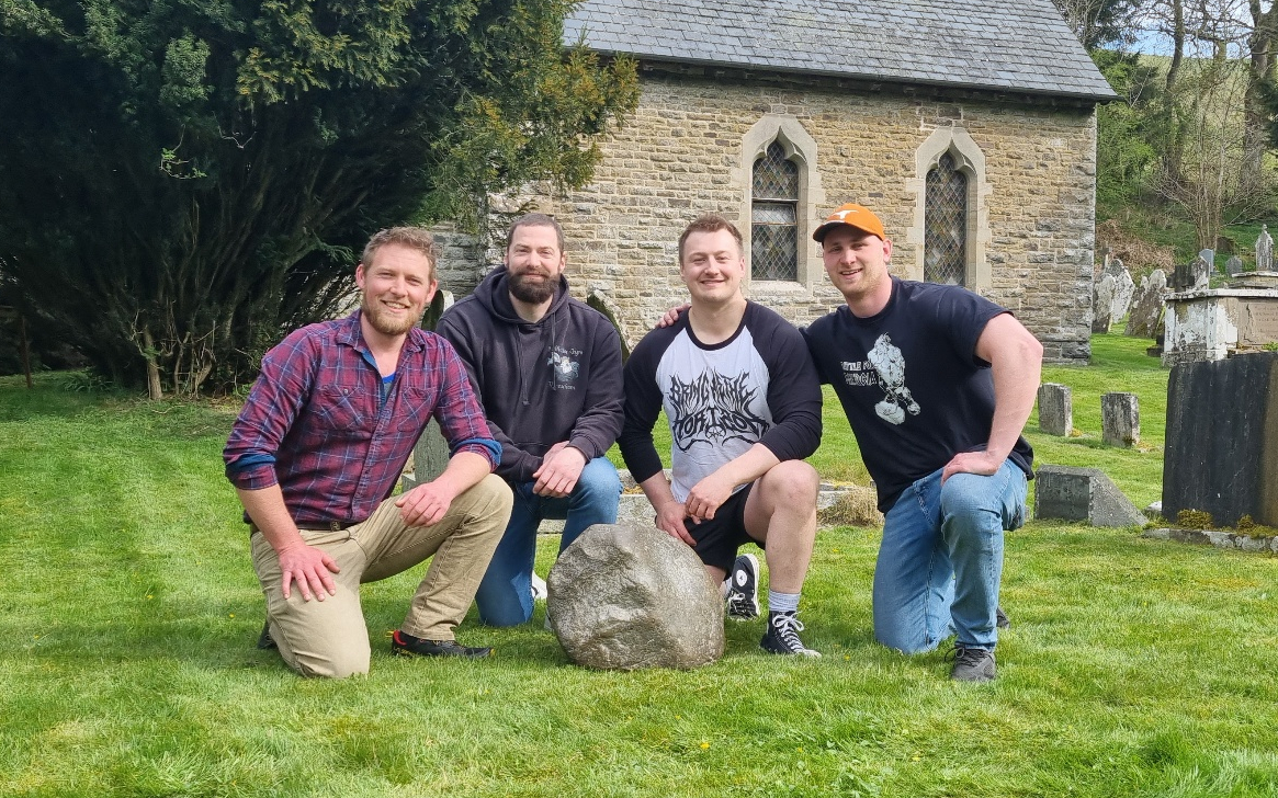 Four men kneeling next to the Maegen Stone in the Mainstone churchyard. From left to right: Calum Stott, Dave Proctor, David Brodlie, Jono Pritchard