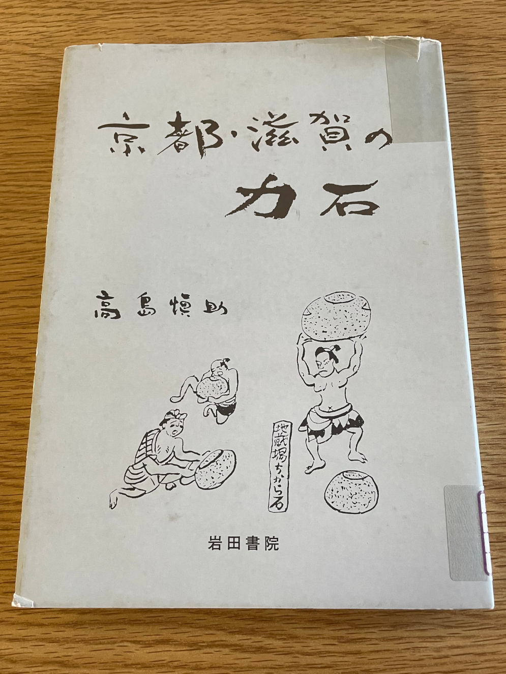 The off-white front cover of Kyoto and Shiga's Power Stones has a few drawings of men lifting stones, it's slightly worn.