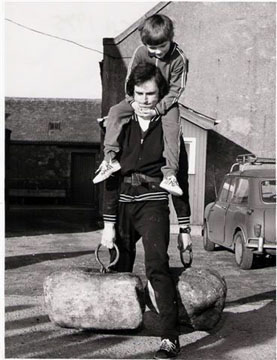 Jim Splaine lifts the Dinnie Stones with his son on his shoulders.