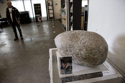 A pedestal inside a bank lobby has holds the 1985 Unspunnen stone on top. There is a small photo of a man throwing the stone beside it.