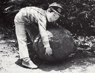 A young boy attempts to lift a large stone.